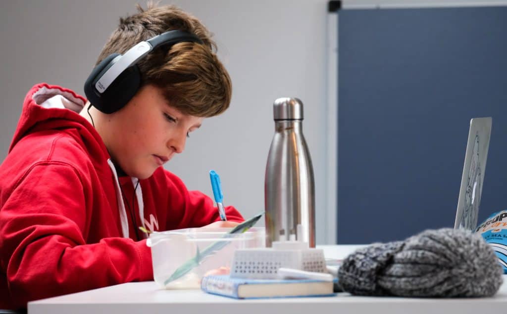 Home schooling during lockdown, boy working on school work with laptop and headphones during coronavirus covid 19 lock down. Remote learning through home schooling due to school closures has become commonplace in the UK in 2021.